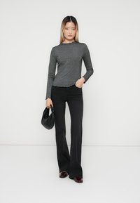 Gray ribbed long-sleeve top with a scalloped neckline, paired with black flared pants and burgundy slip-on shoes, holding a black purse.