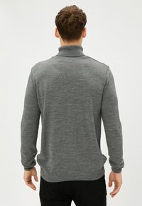 Suéter de punto gris con un cuello alto, puños acanalados y dobladillo. La textura es suave, mostrando el patrón de punto uniforme. Vista posterior.