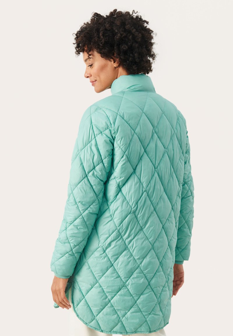 Chaqueta acolchada en azul celeste, con un cuello alto y un patrón de diamantes. La tela parece suave y ligeramente brillante, con mangas largas.