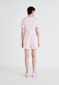 Kortermet rosa og hvit rutete rompers med en tettsittende bodice og shorts. Har en belte detalj bak. Kombinert med blå og rosa platåsko.