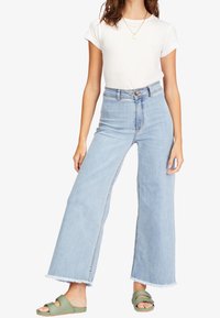 Jeans de tiro alto de color azul claro con dobladillo deshilachado, hechos de denim, con un corte relajado de pierna ancha y cierre frontal de botón.