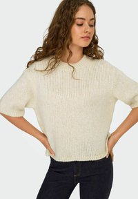 Cremefarvet strikket sweater med korte ærmer, rund halsudskæring og loose fit. Teksturen er blød og en smule chunky, med en ribbet kant.