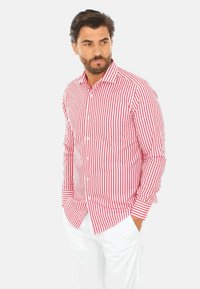 Camicia a righe rosse e bianche con maniche lunghe, fit sagomato, con colletto e polsini. Indossata con pantaloni bianchi.