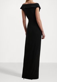 Abito nero senza spalline con silhouette aderente, design fino al pavimento, texture sottile e dettaglio al collo con volant.