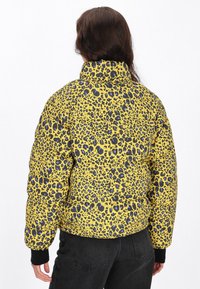 Pohodlná žlutá bunda s černofialovým leopardím potiskem, vysokým límcem a černými manžetami. Zadní strana se vyznačuje prošívaným designem.