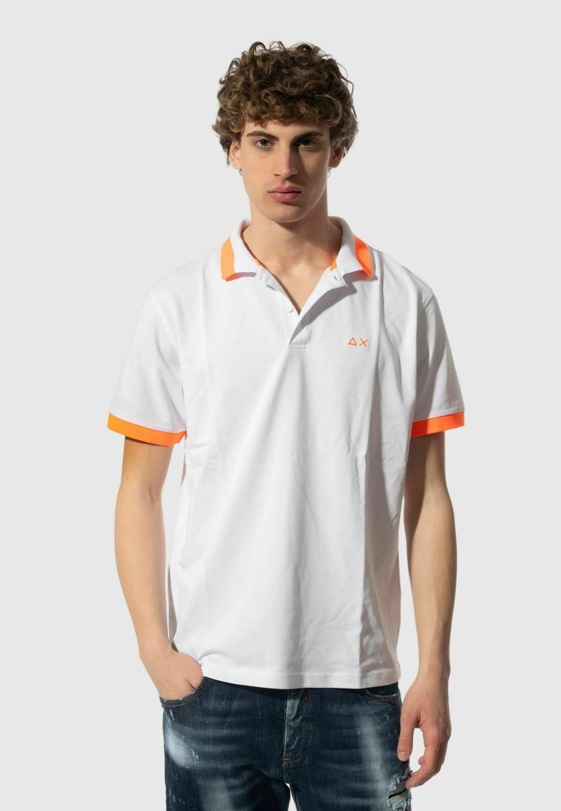 Maglietta polo bianca con accenti arancioni sul colletto e sulle maniche, con un piccolo logo sul petto. Tessuto morbido e vestibilità classica.