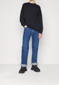 Schwarzer Baumwoll-Sweatshirt mit geripptem Halsauschnitt, kombiniert mit hellblauen Jeans mit umgeschlagenen Säumen und schwarzen Sneakers. Einfaches, lässiges Outfit.