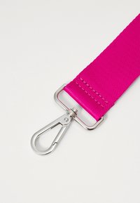 Rosa nylonrem med en glansig silvermetallklämma. Remmen har en texturerad, sydd detalj nära kläms fastsättning.