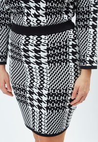 Strikket blyantskirt med et sort og hvidt geometrisk mønster med varierende design, et sort elastisk taljebånd, og en stilren, tætsiddende form.