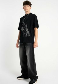 Czarny t-shirt z grafiką psa w połączeniu z luźnymi czarnymi dżinsami. Stylizacja uzupełniają czarne trampki.