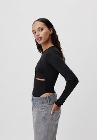 Černý bodysuit s dlouhým rukávem a výřezy, spárovaný s vysokými světlými džíny z denimu. Hladká textura a přiléhavý střih.