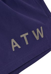 Nahaufnahme eines marineblauen Stoffs mit grauen reflektierenden Buchstaben "ATW", die nahe der genähten Saumkante aufgedruckt sind.