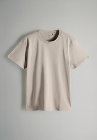 Bež bombažna majica s kratkimi rokavi in okroglim izrezom, gladke teksture. Ima minimalne šive in sproščen kroj.