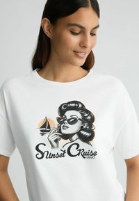 Balta medvilninė marškinėliai su grafiniu atvaizdu, vaizduojančiu moterį akinių nuo saulės retro stiliumi, kartu su valtimi ir užrašu "Saulėlydžio kruizas".