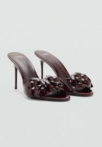 Mules à talons hauts en cuir verni bordeaux avec un design floral à l'avant et un bout ouvert. Texture lisse et brillante avec des talons fins.