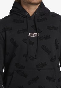 Felpa nera con cappuccio caratterizzata da un motivo testurizzato con il nome del marchio "Billabong" in diverse orientazioni e un logo centrale. Cappuccio con cordoncino.