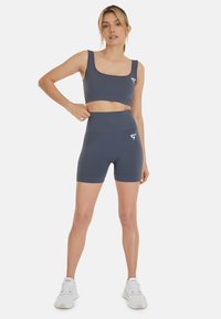 Reggiseno sportivo grigio scuro e pantaloni corti a vita alta in tessuto a costine, con un piccolo logo bianco. Abbinate a scarpe da ginnastica bianche.