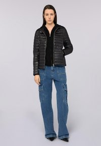 Giubbotto puffer nero con cuciture orizzontali, chiusura con zip e cappuccio; abbinato a jeans cargo blu a gamba larga con tasche laterali.