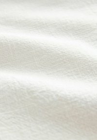 Tessuto bianco con una superficie testurizzata, caratterizzato da sottili motivi e morbidi drappeggi, che mostra un aspetto liscio e leggero.