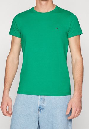 Green cotton t-shirt with short sleeves, round neckline, and small logo on the chest; paired with light blue denim shorts.