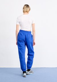 Blaue Jogginghose mit elastischem Bund und Knöchelabschlüssen, kombiniert mit einem weißen cropped T-Shirt und mehrfarbigen Turnschuhen.