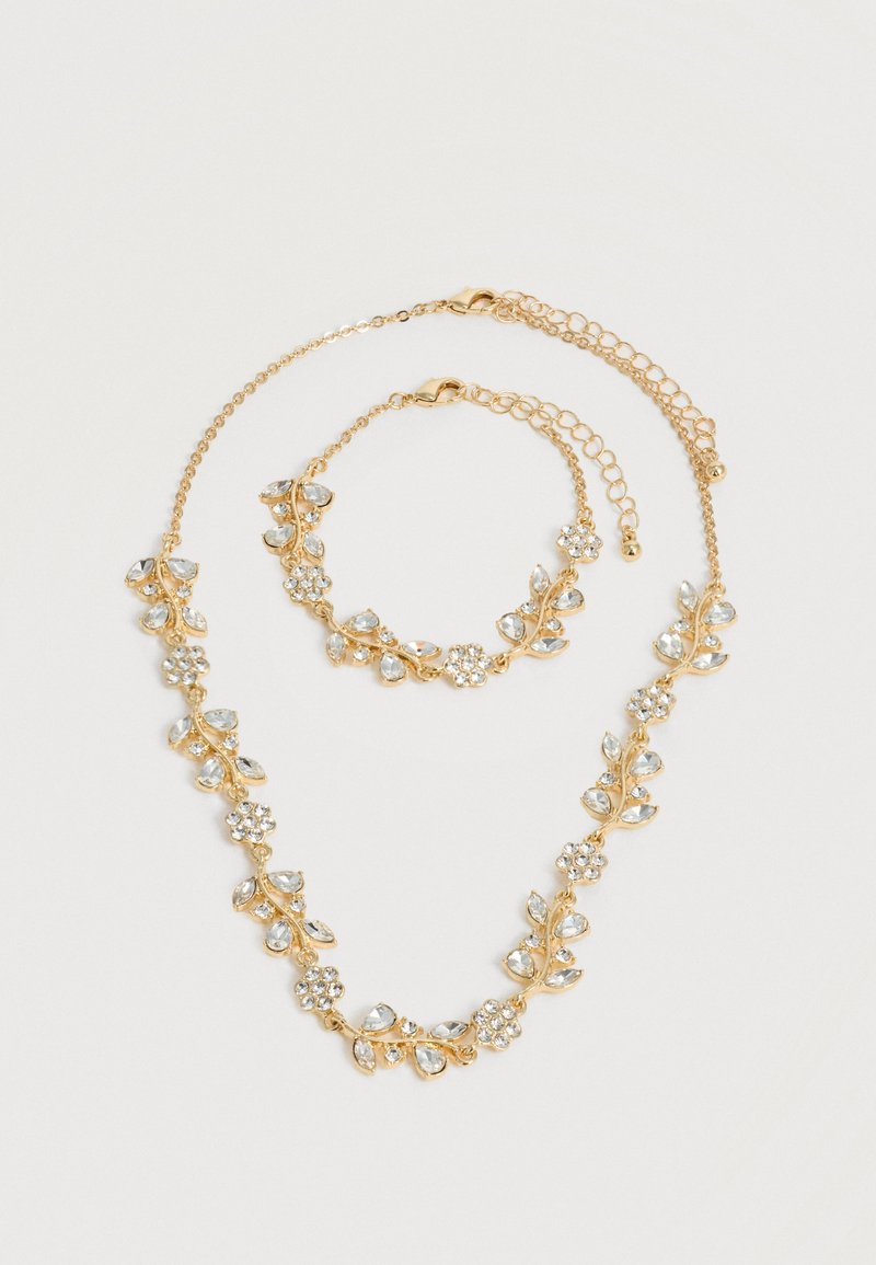 Σετ κολιέ και βραχιόλι σε χρυσό τόνο με διαφανείς κρυστάλλινες λουλουδένιες και φυλλώδεις σχεδιάσεις, και τα δύο με ρυθμιζόμενα κούμπωμα αλυσίδας σε λευκό φόντο.