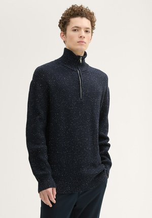 Pull en maille bleu marine avec un col montant et une demi-fermeture éclair. Il présente une texture côtelée avec des éclats multicolores tout au long.