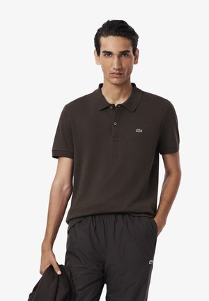 Braunes Poloshirt mit Kragen, kurzen Ärmeln und drei Knöpfen. Mit grünem gesticktem Logo auf der linken Brust.