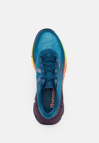 Zapatilla de correr azul con parte superior de malla, acentos en negro y púrpura, suela multicolor y detalles naranjas en la plantilla. Diseño de punta redondeada.