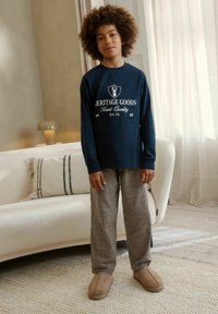 Tumesinine pikkade varrukatega särk valge tekstiga, pruunruudulised püksid ja beežid sussid, omades lõdvestunud istuvust ja pehmet kangatekstuuri.