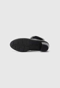 Sandale noire avec une semelle en caoutchouc texturée et une sangle réglable. Présente une forme incurvée avec un profil bas et un détail de marque subtil.