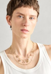 Colliers en or superposés avec divers pendentifs, comprenant une pierre, un charme et des pièces de formes variées. Les chaînes présentent un design de maillons allongés.