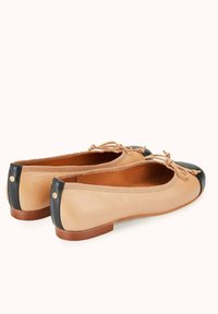 Ballerines en cuir tan avec un bout noir. Elles présentent un petit talon, un détail nœud à l'avant et un panneau arrière texturé.