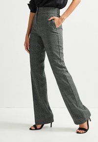 Pantalon taille haute gris à carreaux avec une coupe ajustée, doté de poches latérales et d'une texture lisse; assorti à des sandales noires à talons hauts.