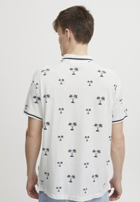 Kortermet poloshirt i hvitt stoff, med et svart palme-mønster, marineblå stripet krage og broderte detaljer.