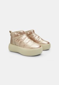 Botas de tobillo metálicas en color oro rosa con parte superior acolchada, paneles laterales elásticos y una gruesa suela de plataforma de color blanco roto. Textura suave, diseño minimalista.