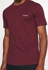 T-shirt in cotone bordeaux con scollatura rotonda, maniche corte e piccolo logo bianco Calvin Klein sulla parte sinistra del petto.