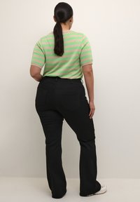 Haut à manches courtes rayé vert et beige associé à un pantalon évasé noir, mettant en avant un design décontracté et une texture de tissu lisse.