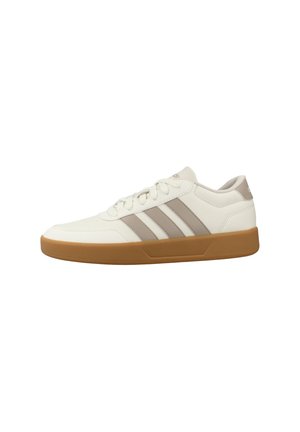 Zapatilla deportiva blanca de perfil bajo con rayas beige y suela de goma, diseño con cordones y collar acolchado para uso casual.