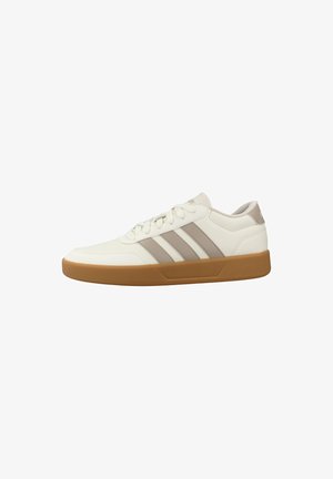 Zapatilla deportiva blanca de perfil bajo con rayas beige y suela de goma, diseño con cordones y collar acolchado para uso casual.