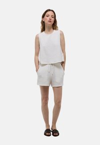 Haut sans manches texturé blanc associé à un short texturé assorti. La tenue présente une coupe décontractée et une taille avec cordon de serrage, complétée par des sandales sombres.