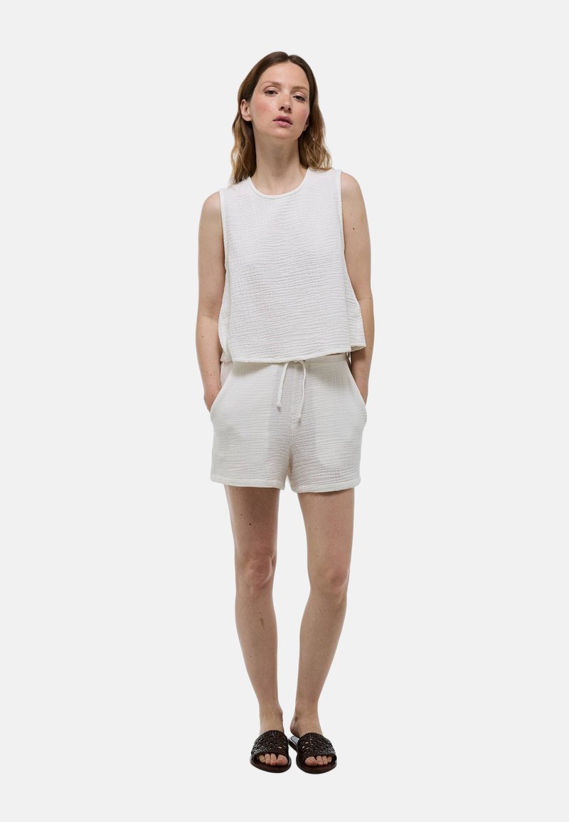 Haut sans manches texturé blanc associé à un short texturé assorti. La tenue présente une coupe décontractée et une taille avec cordon de serrage, complétée par des sandales sombres.