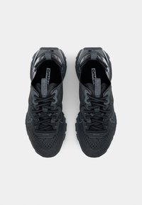 Paire de chaussures de sport noires avec dessus en mesh texturé, fermeture à lacets et languettes siglées, vues de dessus sur un fond uni.
