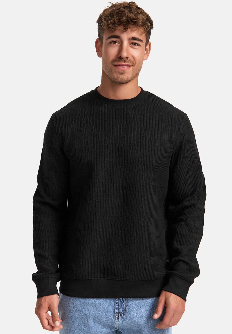Felpa nera a trama con collo rotondo e maniche lunghe, caratterizzata da un motivo sottile. Abbinata a jeans in denim azzurro chiaro.