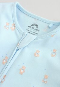 Grenouillère bébé bleu clair avec des ours en peluche imprimés et une fermeture éclair devant, étiquetée "NEXTbaby" avec le texte "garde-moi, aime-moi, transmets-moi."