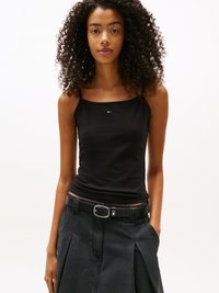 Black tank top with thin straps, featuring a small logo patch. Paired with a high-waisted, pleated black skirt and a black belt with a silver buckle.