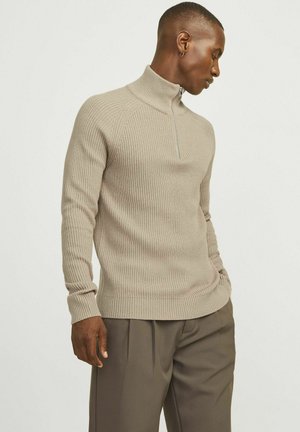 Beige ribbad stickad tröja med hög krage och halvdragkedja, har långa ärmar och en figurnära design. Texturerade tygdetaljer synliga.