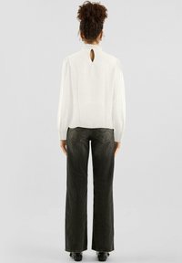 Weiße Bluse mit gerüschtem Ausschnitt und einem Schlüsselloch-Detail am Rücken, kombiniert mit dunklen, weit geschnittenen Jeans. Glatter Stoff mit subtiler Textur.