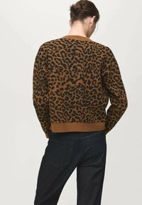 Brown and black leopard print sweater with ribbed neckline and hem, made from a textured material. Worn with dark denim pants.