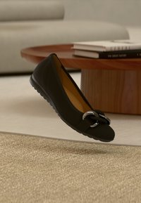 Juodas lygus batelis su sidabrine kilpa priekyje ir tekstūruotu padu sukibimui, nufotografuotas neutraliame fone.